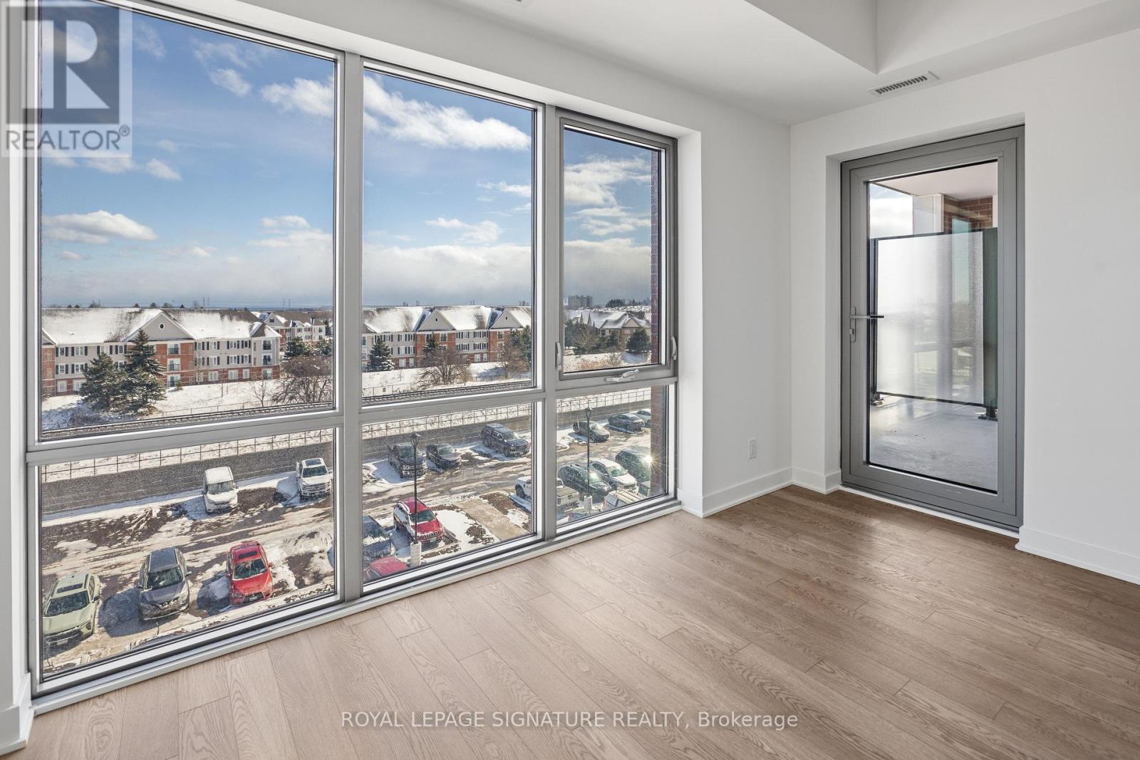 A room with a view of a parking lot and buildings outside.