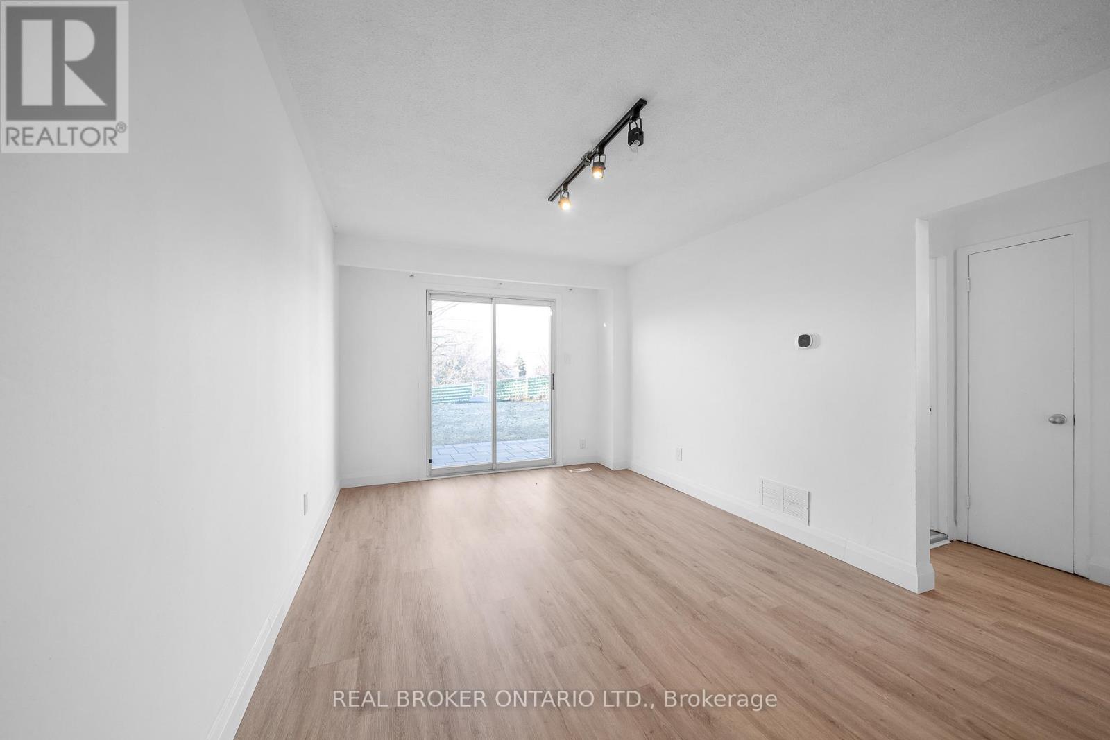 A spacious room with wooden flooring and white walls, with a window overlooking a body of water.