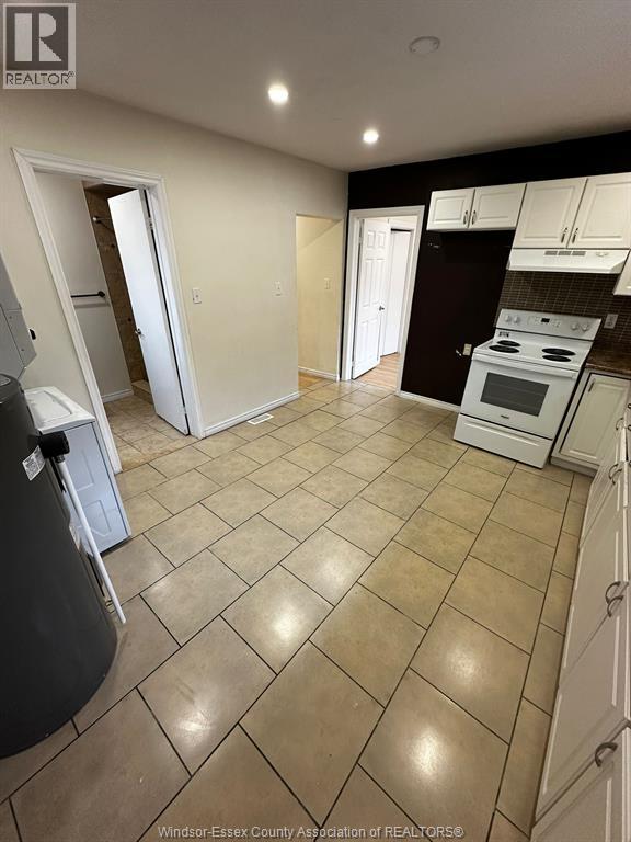 A kitchen with white appliances and a black trash can.