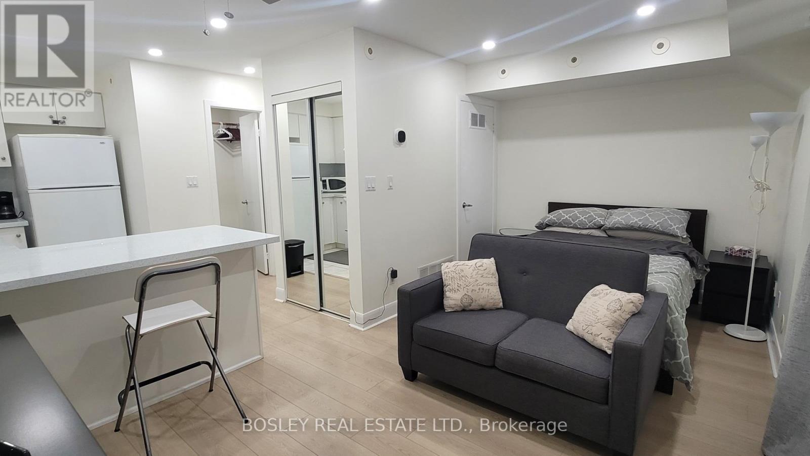 A real estate listing image of a bedroom with a bed, couch, and desk.