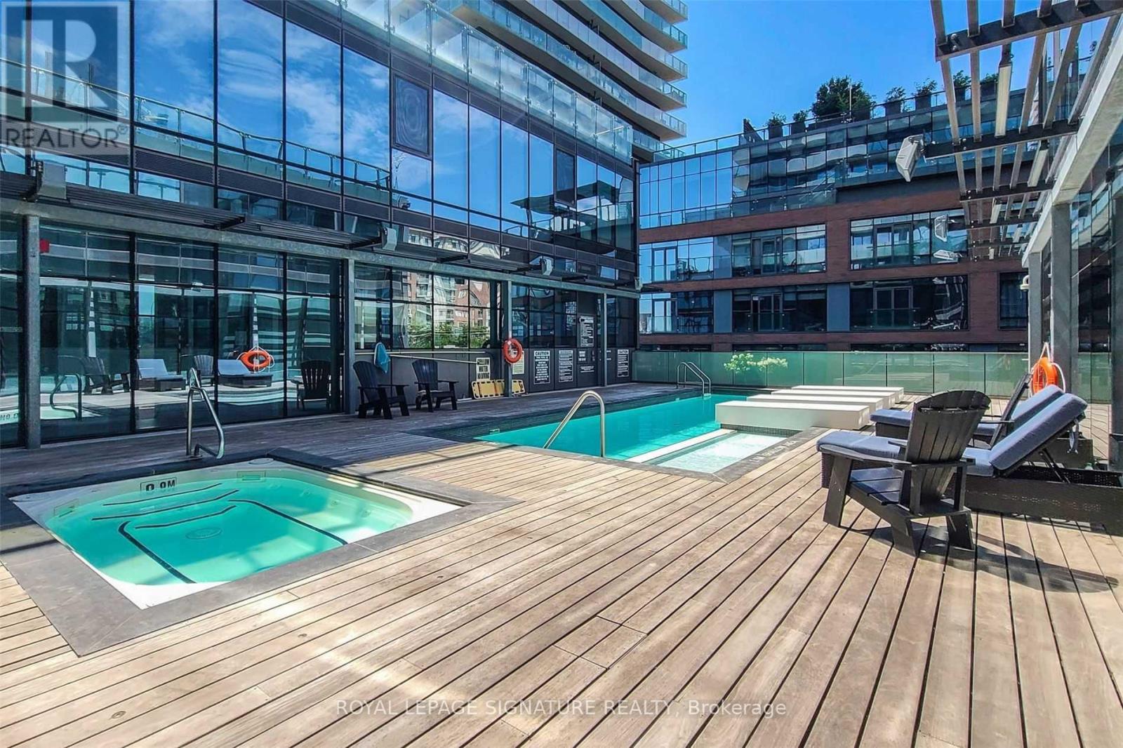 A wooden deck with a pool and chairs in front of a glass building.