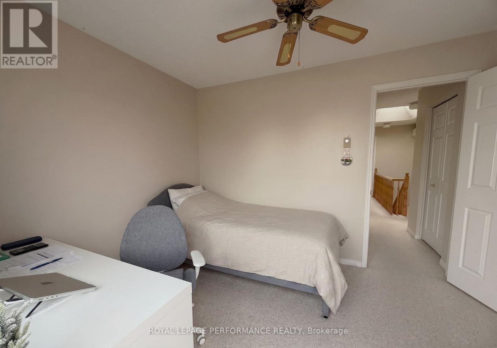 A bedroom with a bed, a ceiling fan, and a laptop on a table.
