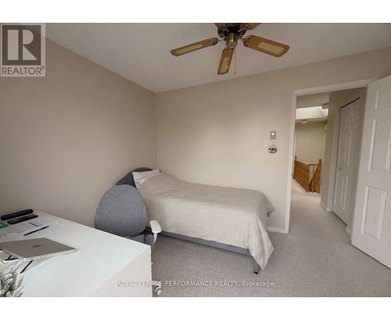 A bedroom with a bed, a ceiling fan, and a laptop on a table.