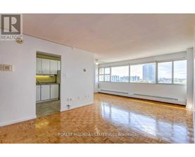 A spacious room with wooden flooring and a view of the city through large windows.