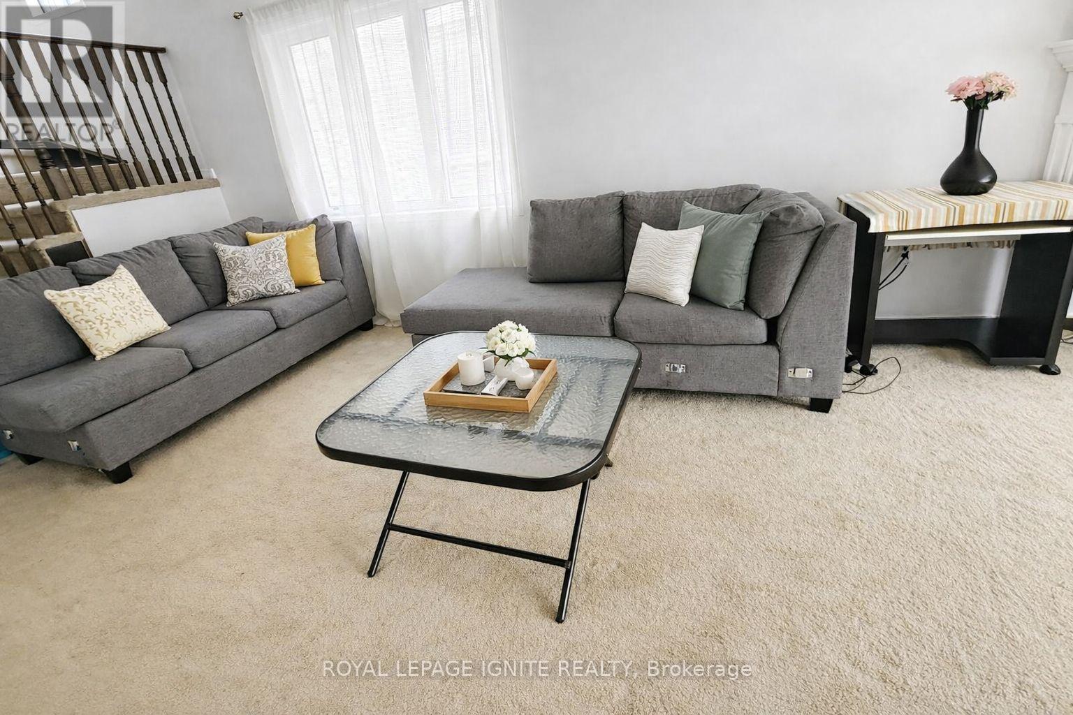 A living room with two grey couches, a glass coffee table, and a small table with a vase of flowers.
