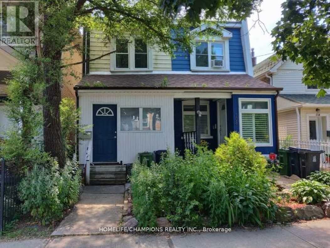 A blue house with a white door and windows is surrounded by greenery.