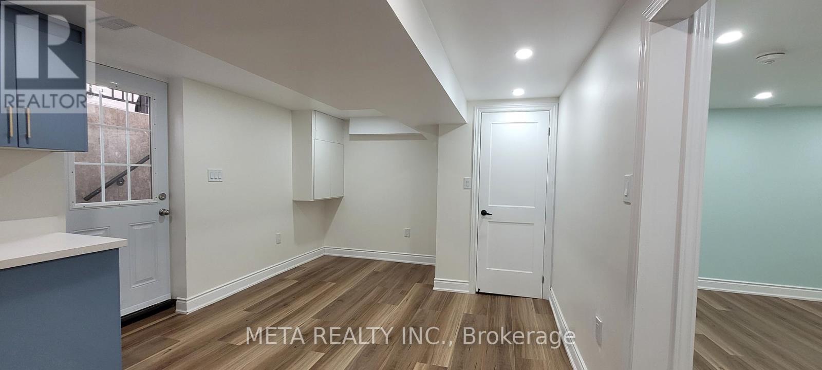 A real estate listing photo of a room with wood floors and white walls.