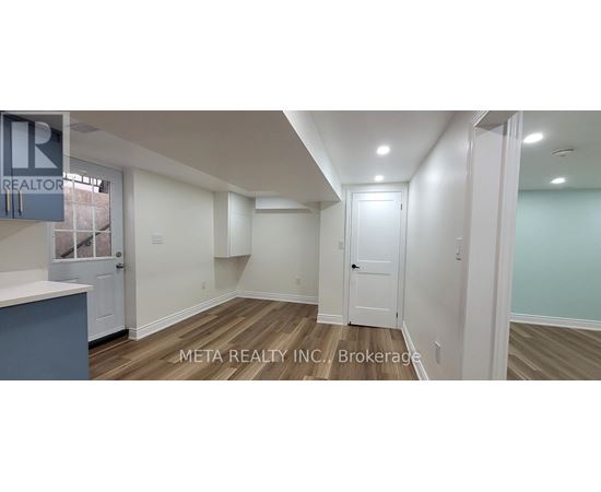 A real estate listing photo of a room with wood floors and white walls.
