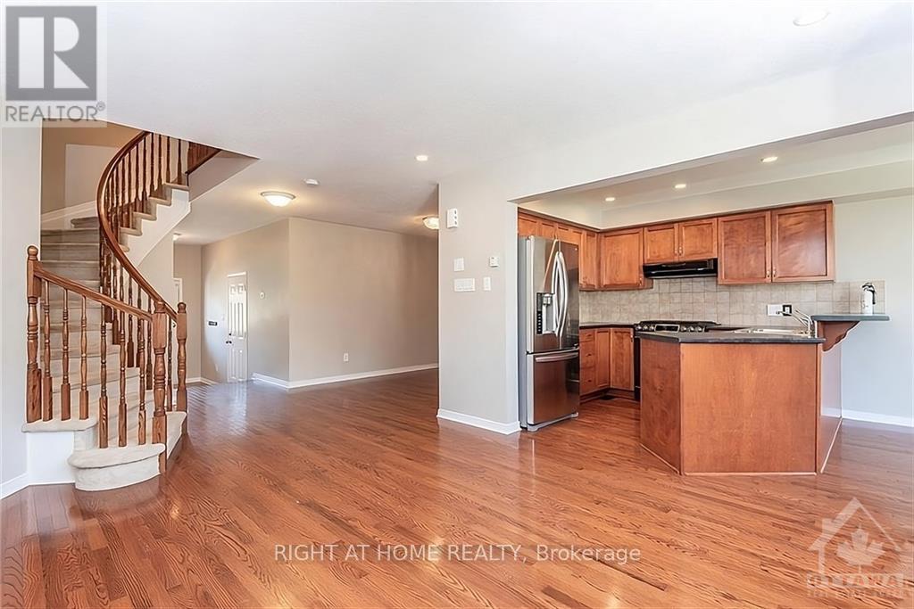 A well-lit kitchen with wooden cabinets and a staircase on the left side.