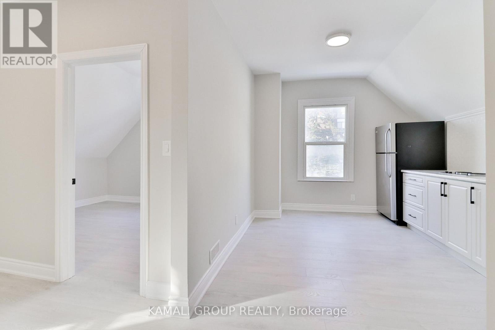 A white room with a kitchen area to the right and a doorway leading to another room.