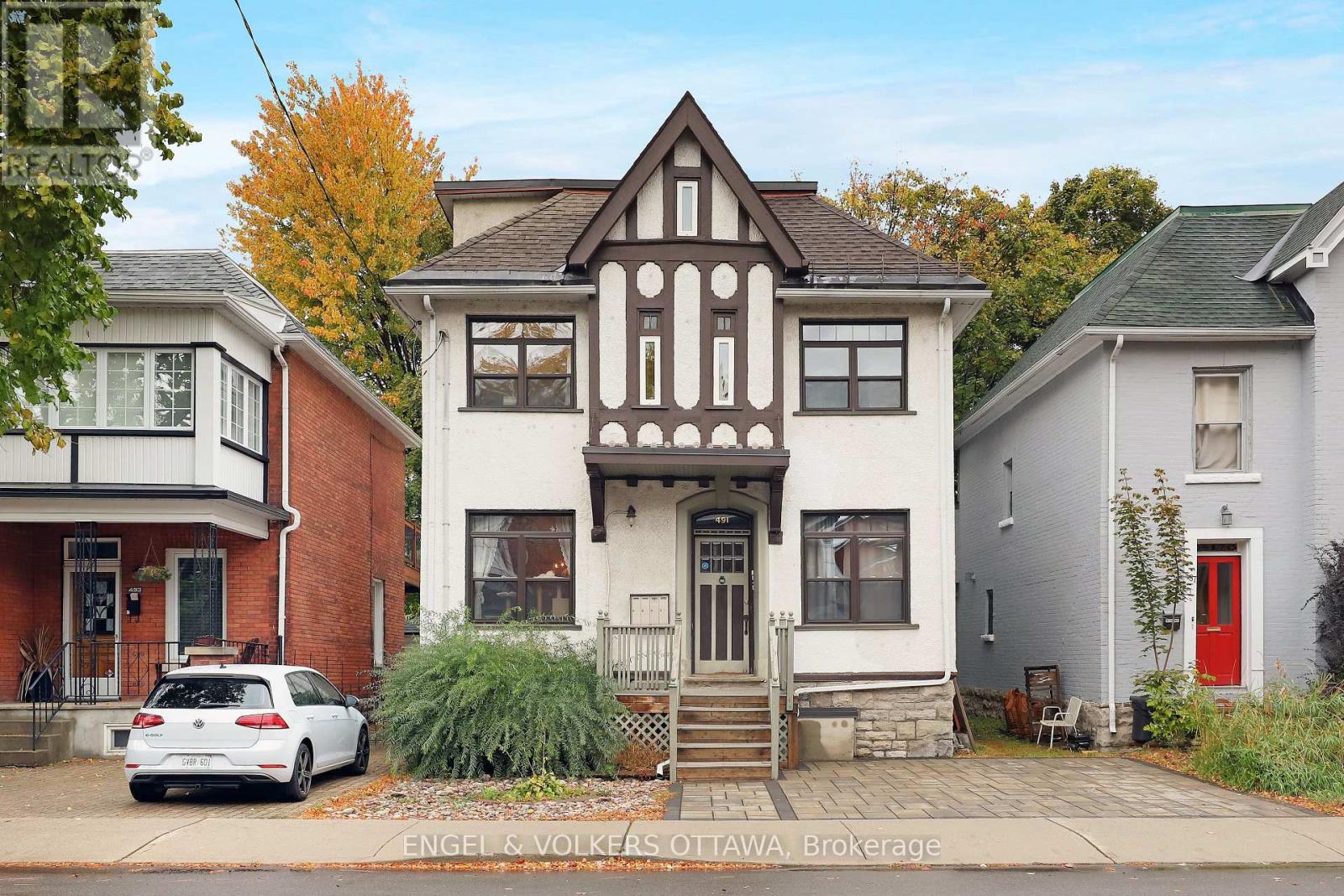 A white car is parked in front of a house with a red door.
