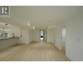 A spacious room with wooden floors and white walls, with a brokerage sign for CITYSCAPE REAL ESTATE LTD.