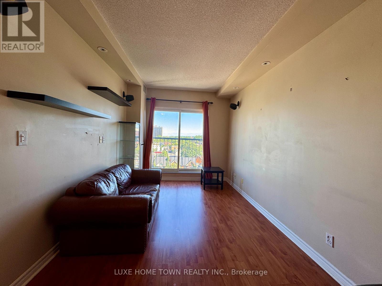 A living room with a brown leather couch and a window with red curtains.