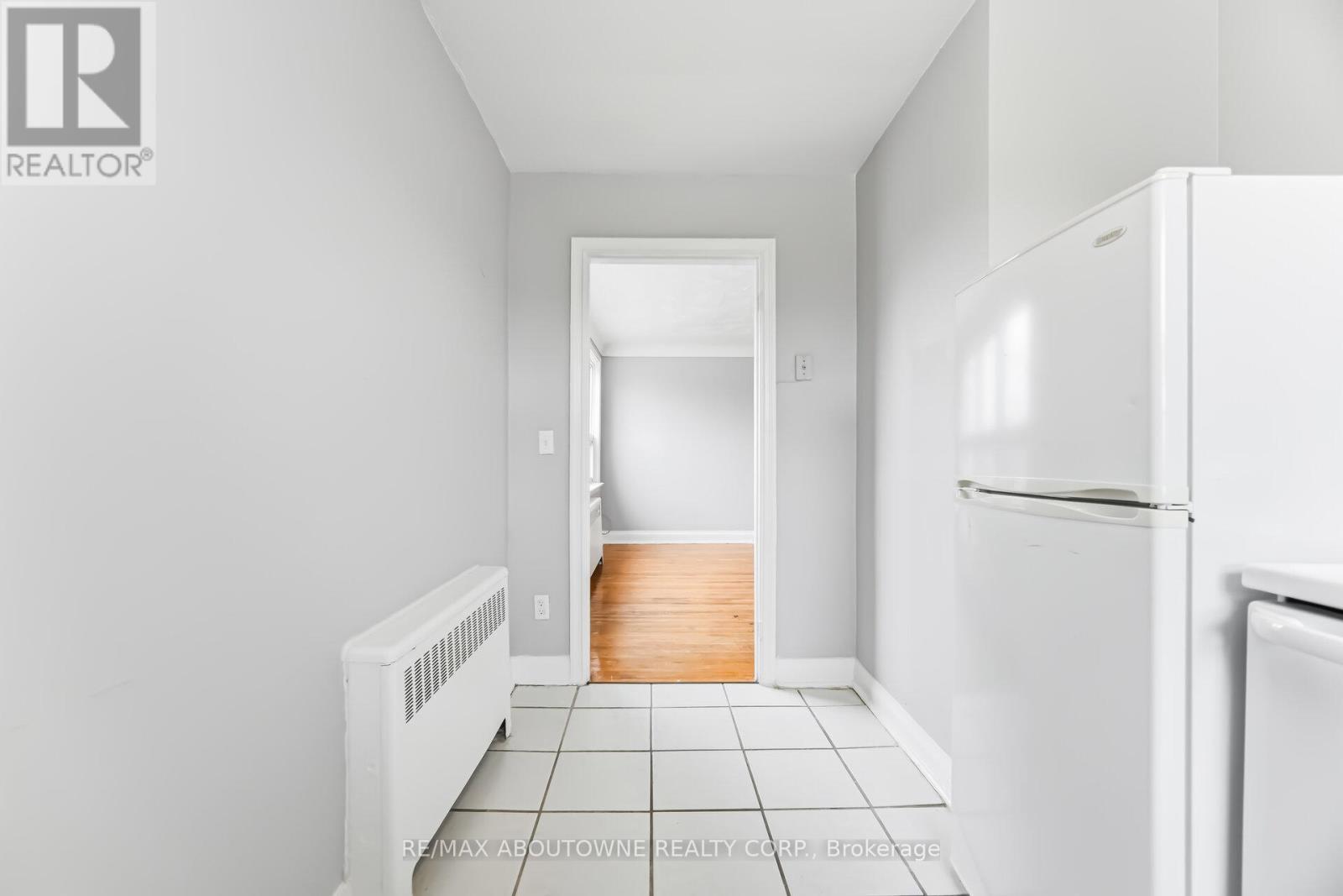 A white refrigerator sits in a kitchen with white walls and tile flooring.