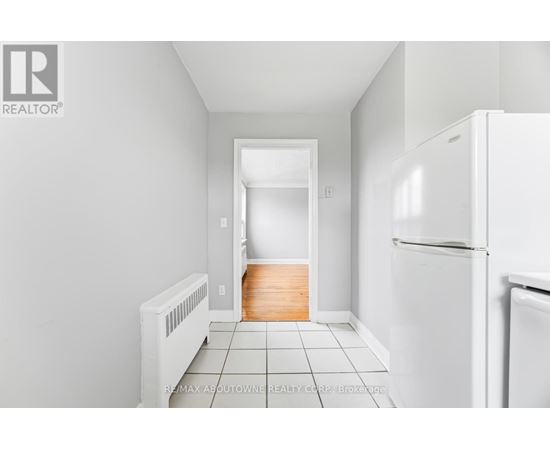 A white refrigerator sits in a kitchen with white walls and tile flooring.