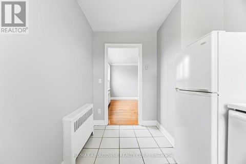 A white refrigerator sits in a kitchen with white walls and tile flooring.