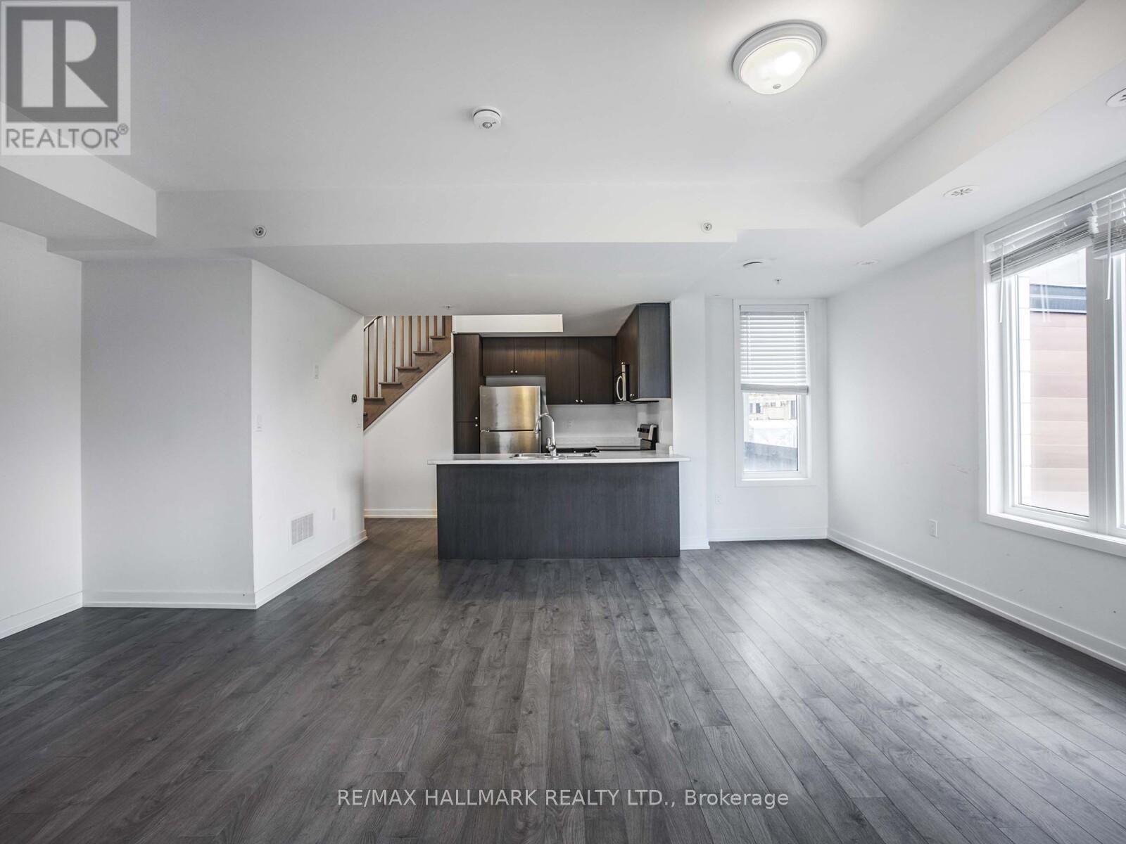 A spacious room with wooden floors and a staircase leading to the upper level.