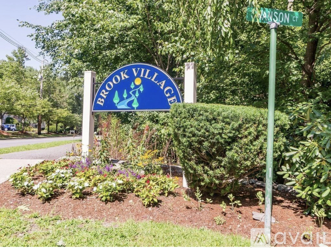 A Brook Village sign is in front of a green bush.