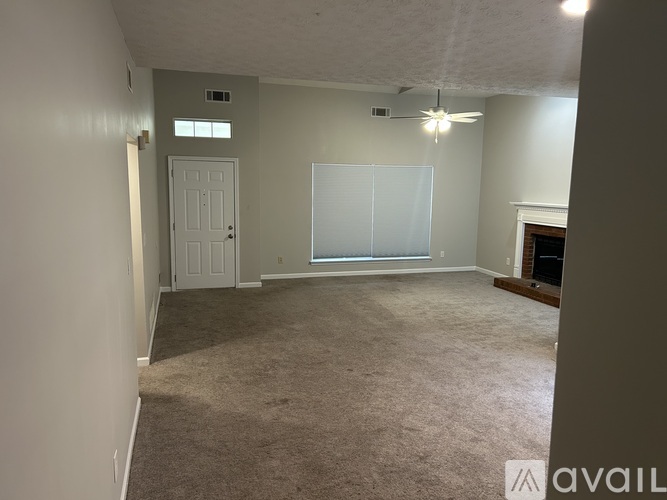 A room with a carpeted floor, a ceiling fan, and a door.