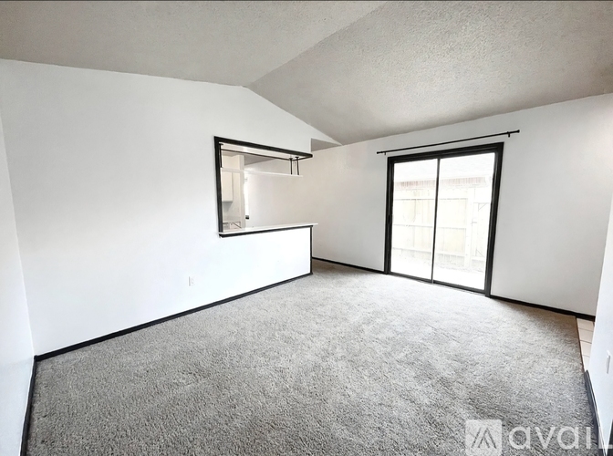 A room with a grey carpet and a window with a white frame.