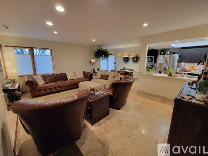 A living room with brown leather furniture and a kitchen area in the background.