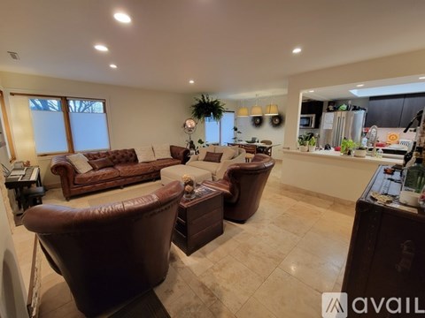 A living room with brown leather furniture and a kitchen area in the background.