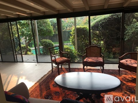 A living room with a round table and chairs with a view of a garden outside.