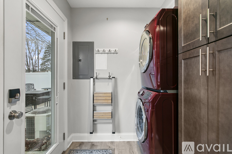 A red washing machine is in a laundry room with a view of trees outside.