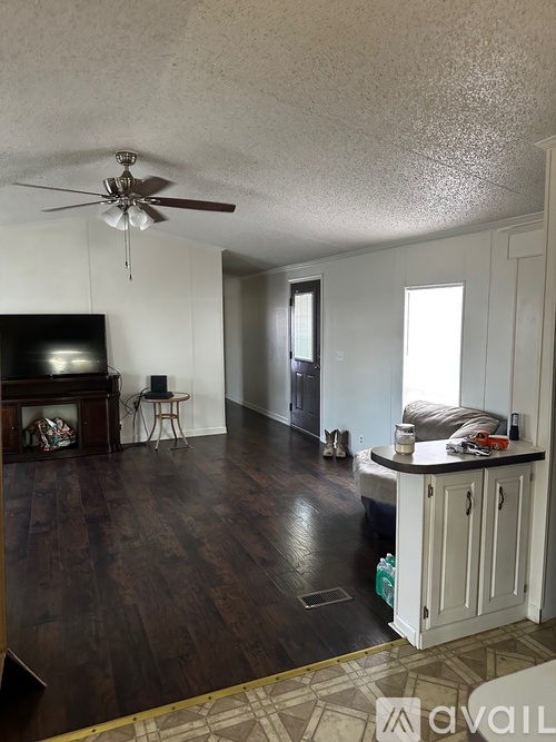 A living room with a brown ceiling fan and dark wood floors.
