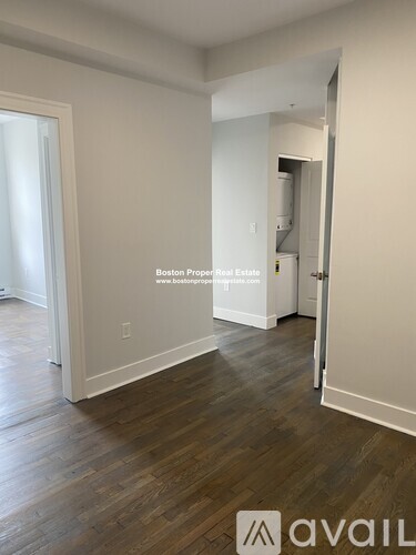 A room with wooden flooring and white walls, with a doorway leading to another room.
