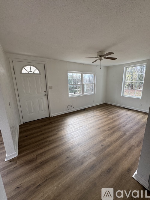 A room with a white door, a ceiling fan, and two windows.