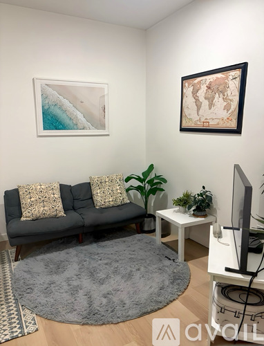 A living room with a grey couch, a grey rug, a white table, a television, and two framed pictures on the wall.