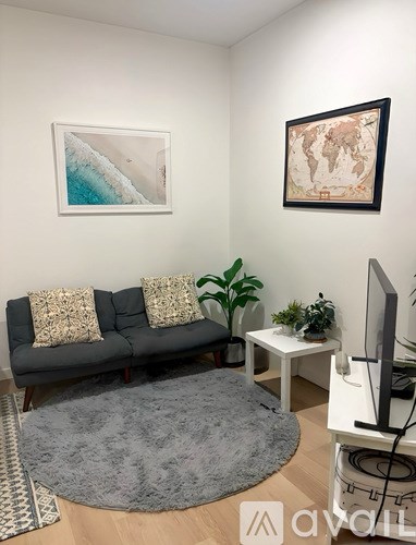A living room with a grey couch, a grey rug, a white table, a television, and two framed pictures on the wall.