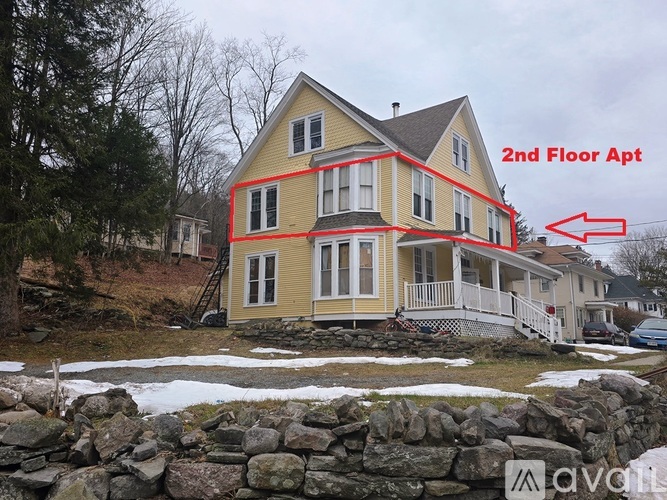 A house with a stone wall in front and a red arrow pointing to the second floor attic.