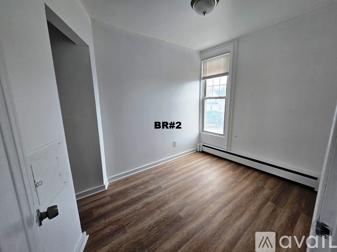 A room with wooden flooring and a window with a view of a building outside.