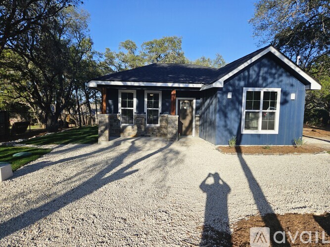 A blue house with a gravel driveway and trees in the background.