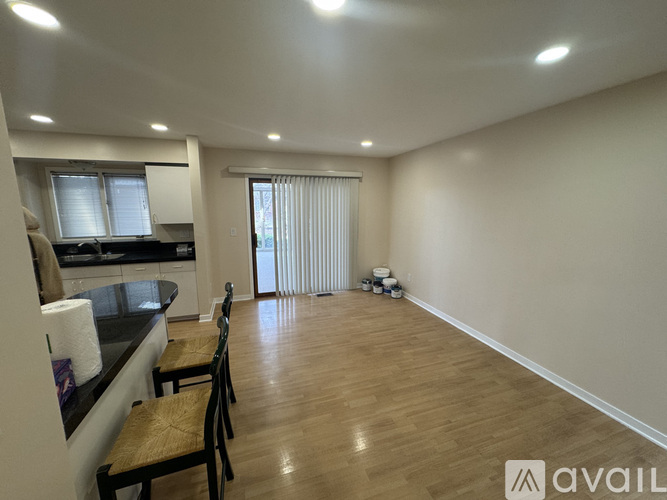 A room with wooden flooring and a kitchen area with a counter and chairs.