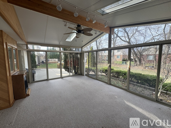 A spacious room with a ceiling fan and large windows overlooking a garden.