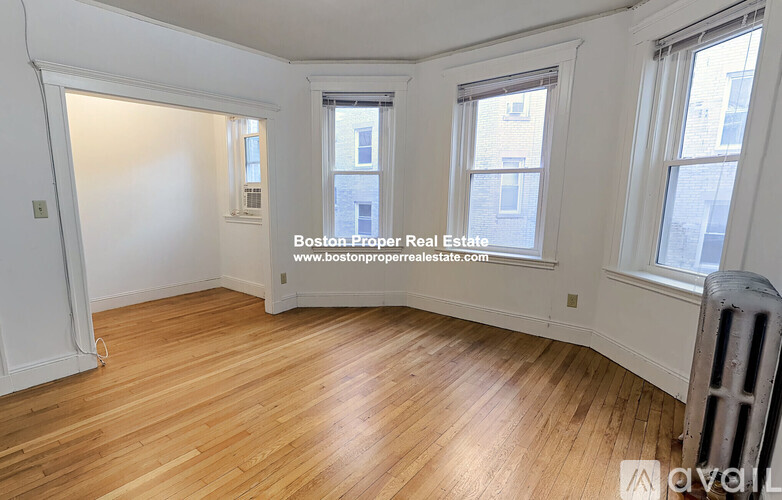 A room with wooden flooring and three windows.