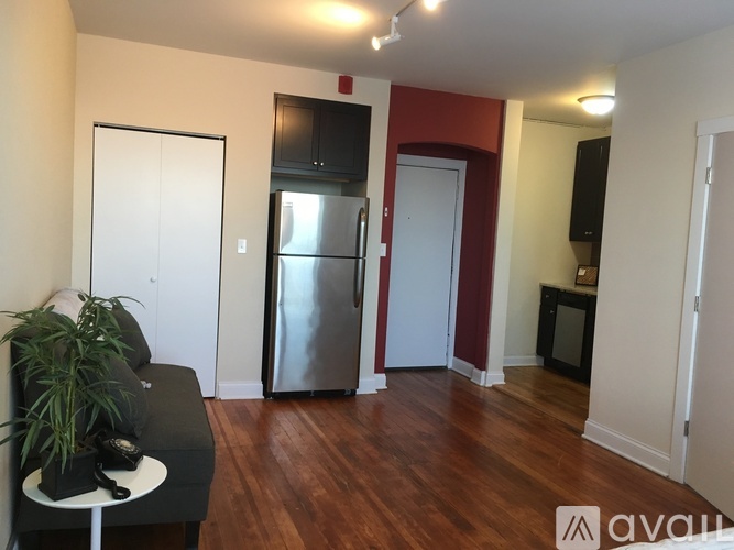 A kitchen area with a refrigerator, a black sofa, and a potted plant.
