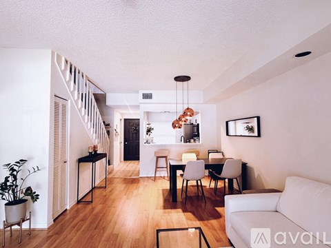 A living room with a white couch, a dining table with chairs, and a staircase with a railing.