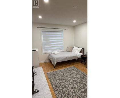 A bedroom with a bed, a window with blinds, and a rug on the floor.