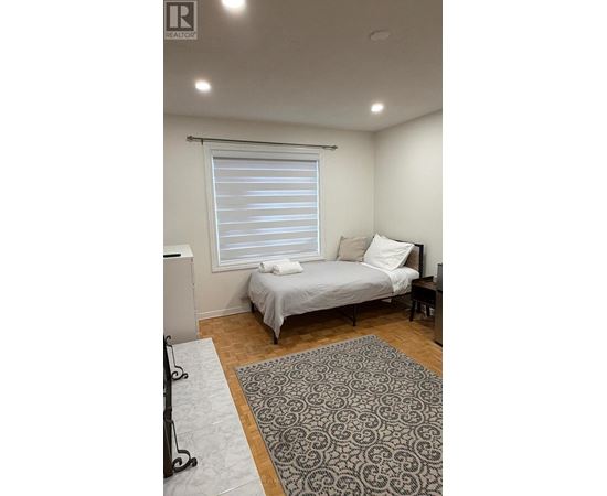 A bedroom with a bed, a window with blinds, and a rug on the floor.