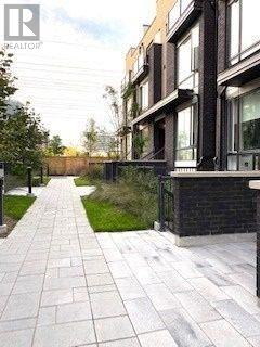 A long, narrow walkway with a brick pattern is flanked by modern buildings.