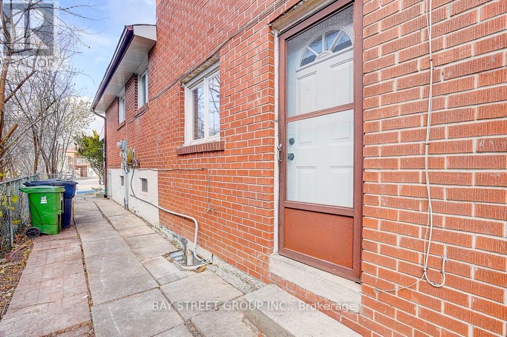 A red brick house with a white door and a green trash can.