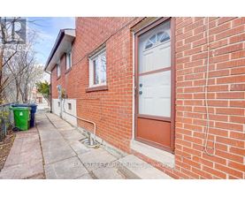 A red brick house with a white door and a green trash can.