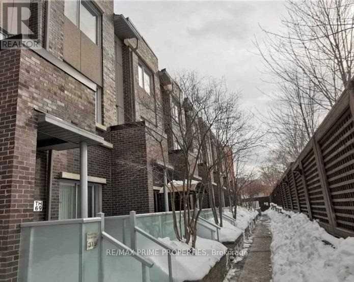 A snowy pathway leads to a brick building with a sign that reads "RE/MAX Prime Properties, Brokerage.".