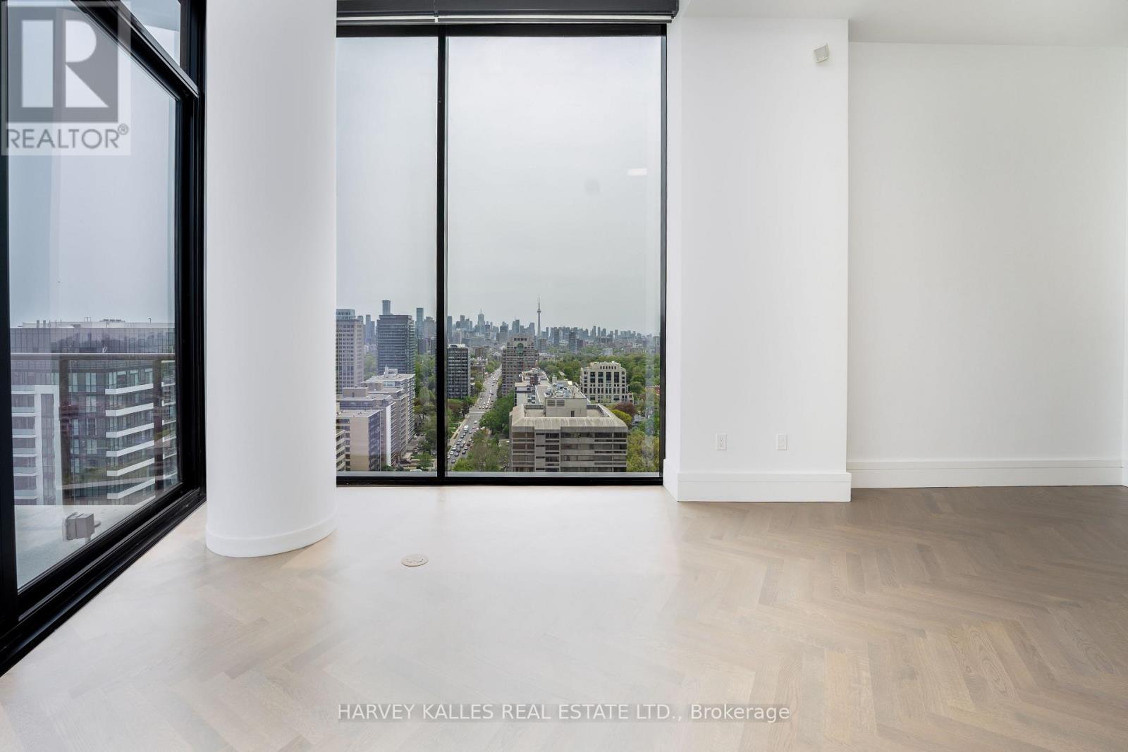 A real estate listing photo of a large empty room with a view of the city.