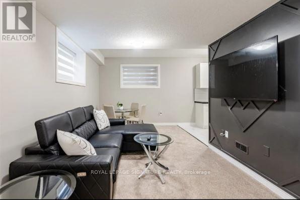 A living room with a black leather couch and a flat screen TV mounted on the wall.