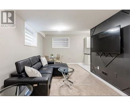 A living room with a black leather couch and a flat screen TV mounted on the wall.